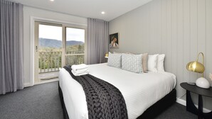 A hotel room with a bed, a nightstand, a lamp, a painting, and a view of the outdoors.