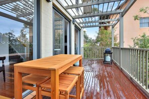 Una terraza de madera con una mesa, bancos, barandilla y vistas del entorno.