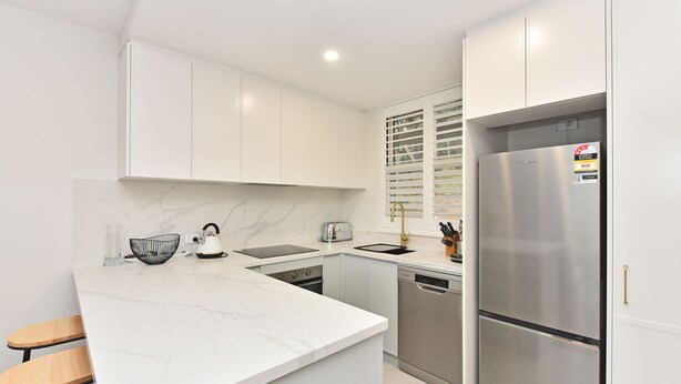Una cocina moderna con armarios blancos, un refrigerador de acero inoxidable, horno empotrado y lavavajillas.