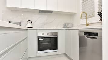 A modern kitchen with white cabinetry, a built-in oven, a dishwasher, and a kettle on the countertop.