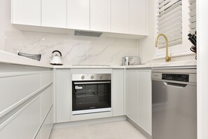 Una cocina moderna con armarios blancos, horno empotrado, lavavajillas y tetera sobre la encimera.