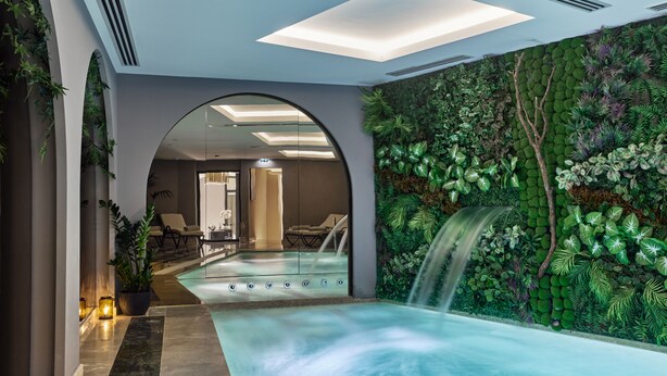 Een wellnessruimte met een jacuzzi, een watervalmuur en een zithoek met stoelen en een tafel.