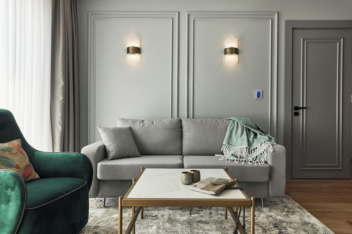 Ein modernes Wohnzimmer mit grauem Sofa, einem grünen Sessel, einem Marmortisch und zwei Wandleuchten.