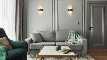 Ett modernt vardagsrum med en grå soffa, en grön fåtölj, ett soffbord i marmor och två väggmonterade lampor.