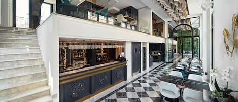 Un hall d’hôtel moderne avec un sol à carreaux, un espace bar et un escalier menant à un étage supérieur.