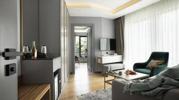 A modern living room with a sofa, coffee table, and a TV. There is a kitchen area with a countertop and cabinets.