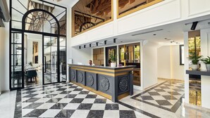 Eine Hotelhalle mit Schachbrettfußboden, einer Rezeption und einer Treppe, die zu einer oberen Ebene führt.