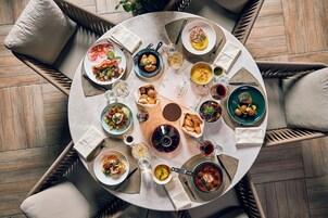 A round dining table with various dishes and drinks, surrounded by wicker chairs.