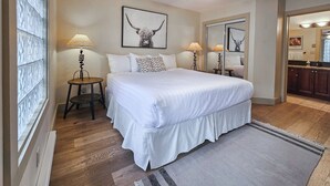 A bedroom with a large bed, two bedside tables with lamps, a ceiling fan, and a mirror. - Pet-Friendly 2-Bedroom Condo Near Hot Springs (Radium Hot Springs)