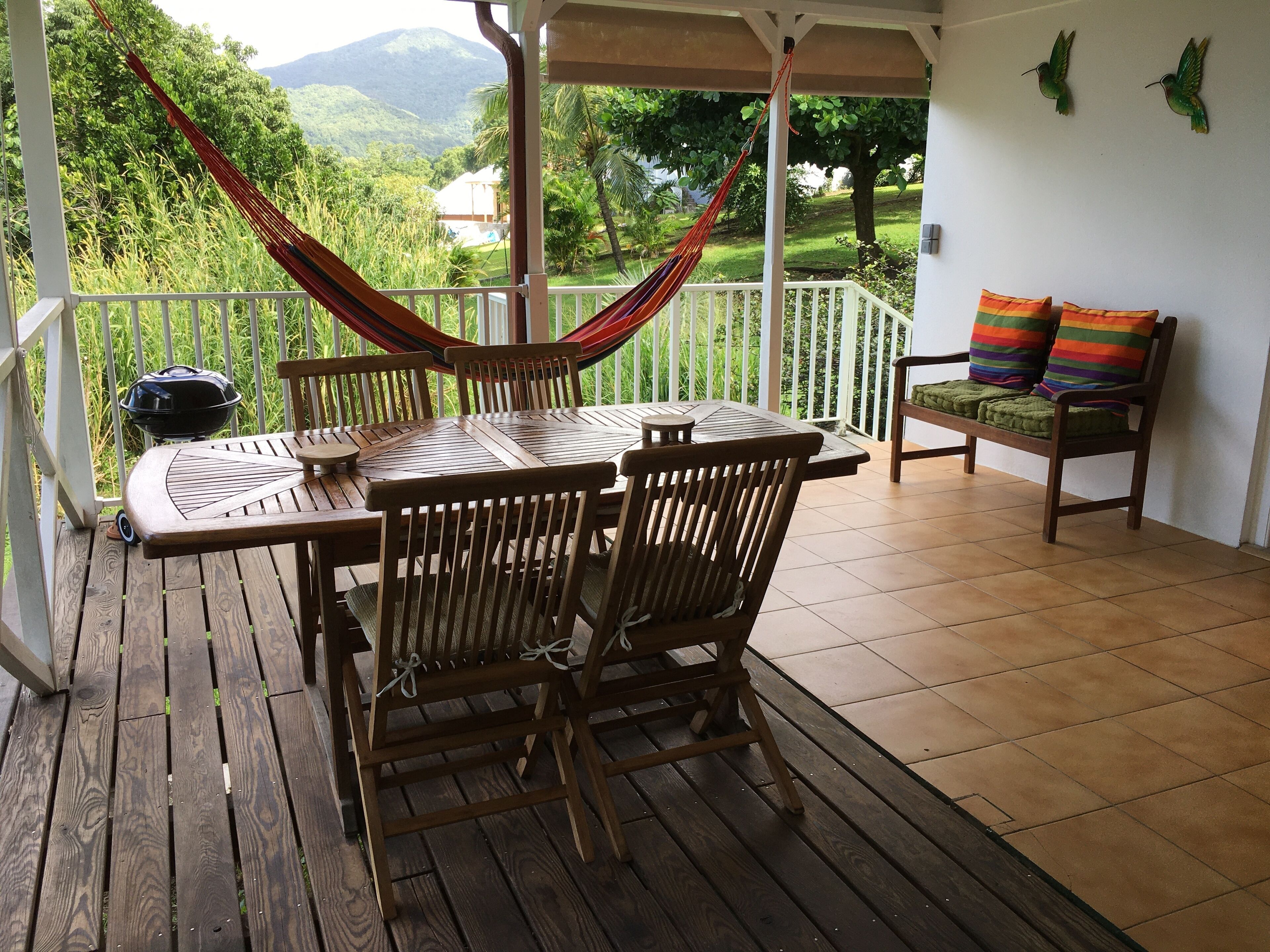 A wooden deck with a table and chairs, a hammock, and a view of greenery and mountains.