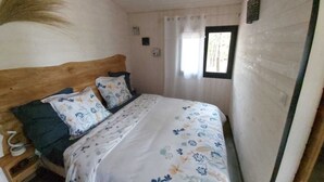 Quarto pequeno e acolhedor com cabeceira de madeira, uma cama de solteiro com roupa de cama floral, mesa de cabeceira e janela com cortinas.