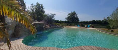 Une piscine dotée d’une terrasse en bois, entourée d’arbres et surplombée par un ciel dégagé.