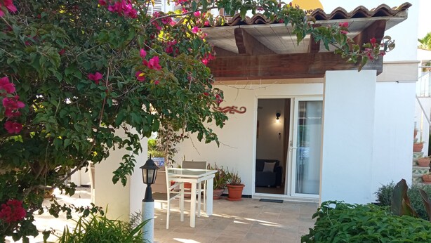 A patio area with a white table and chairs, surrounded by potted plants and a pergola. - CAP DE MAR (Alcudia)