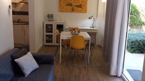 A compact living space with a kitchenette, a dining area with a table and chairs, a sofa, and a large window with curtains. - CAP DE MAR (Alcudia)