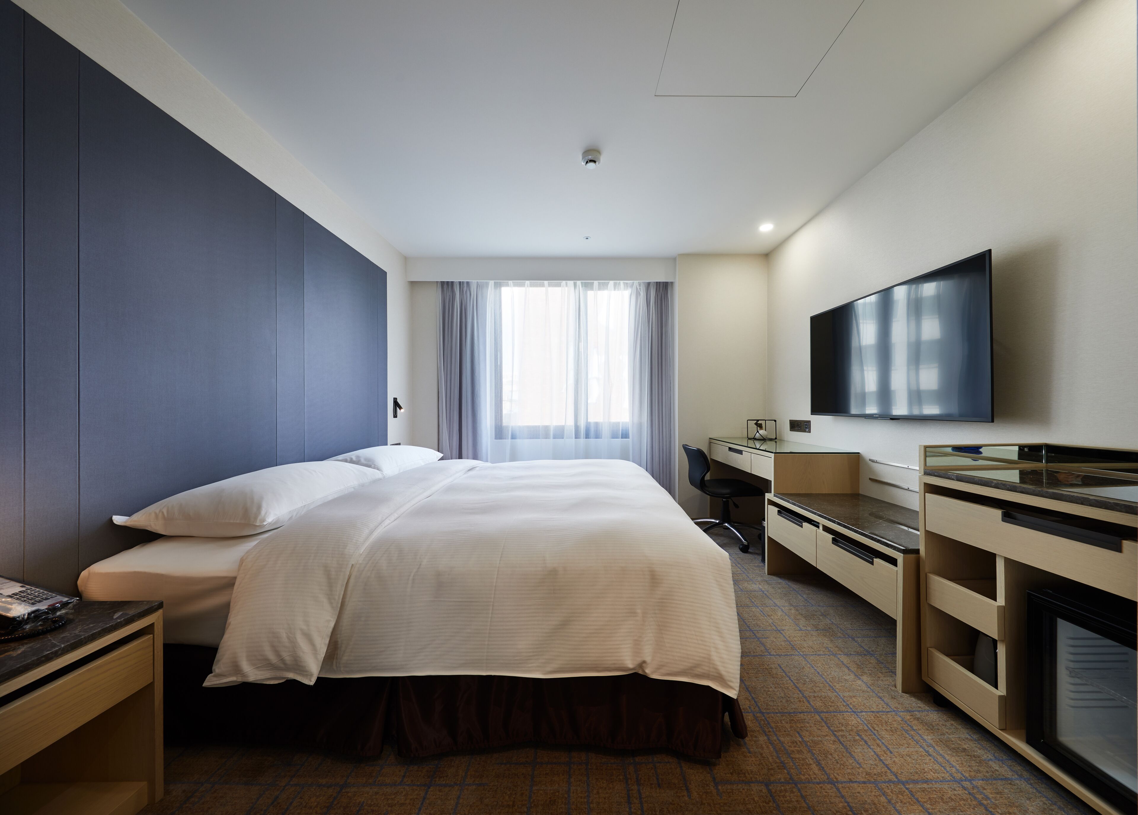 Ein Hotelzimmer mit einem großen Bett, einem Schreibtisch, einem Flachbildfernseher und einem Fenster mit Vorhängen.