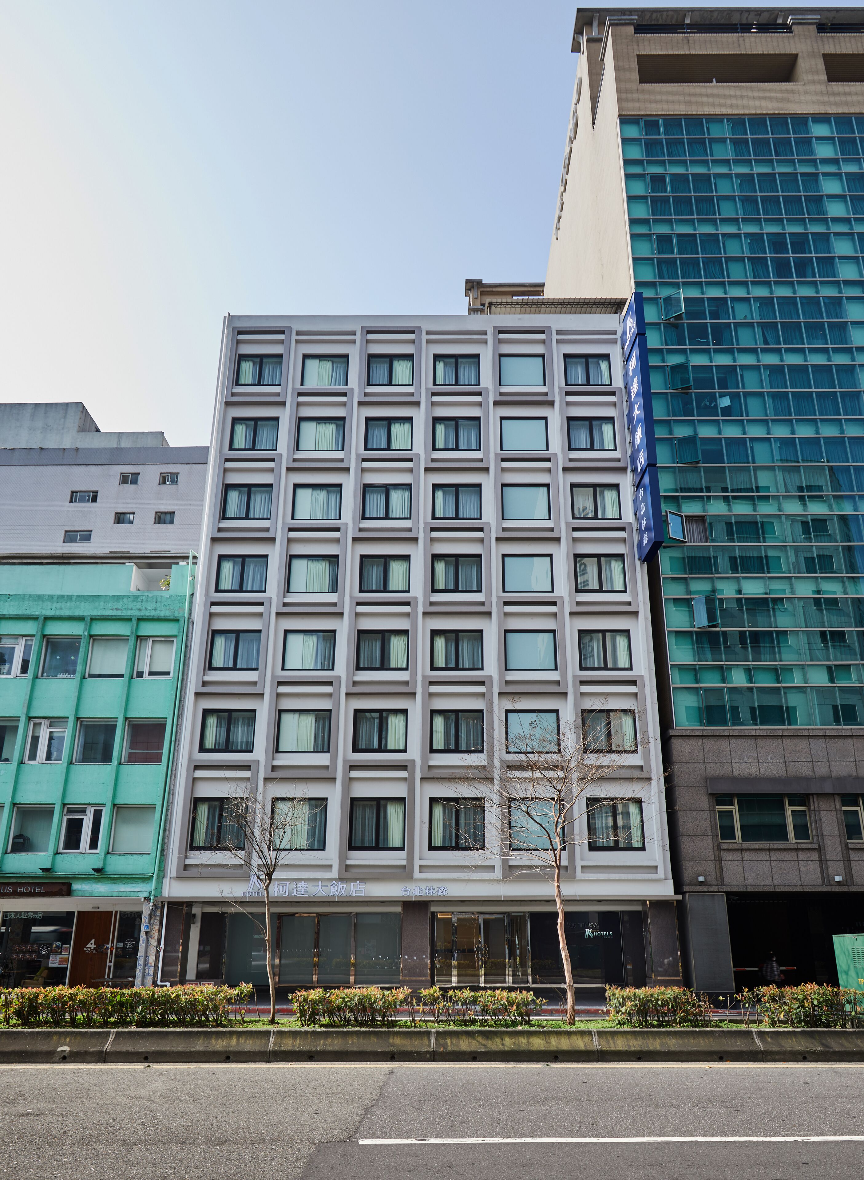 Een meerlaags hotel met een moderne gevel, met een symmetrisch raam patroon en een opvallend blauw bord aan de rechterkant.
