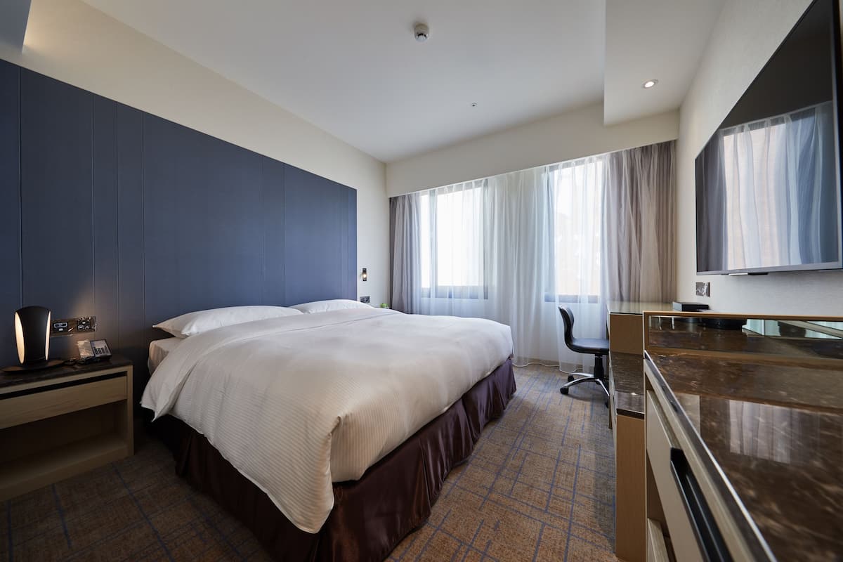 A modern hotel room with a large bed, a desk, a chair, and a TV.