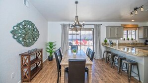 A dining area with a wooden table, chairs, a chandelier, and a view of the outdoors. - LUXURY Living 2 (Yuma)
