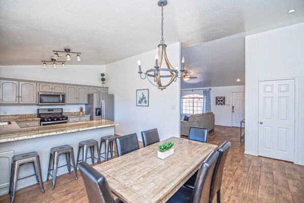A spacious kitchen with modern appliances, a dining area with a wooden table and bar stools, and a living area with a sofa and a large window.