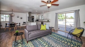 A modern living room with a grey sofa, a dining table, and a kitchen in the background. - LUXURY Living 3 (Yuma)