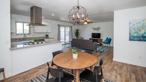 A modern kitchen with white cabinets, a stainless steel range hood, and a dining area with a round wooden table and black chairs. - LUXURY Living 3 (Yuma)