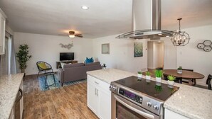 A modern kitchen with a built-in oven, a dining area with a round table, and a living room with a sofa and television. - LUXURY Living 3 (Yuma)