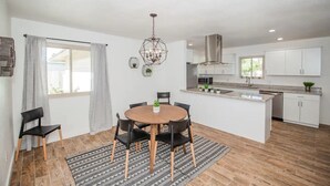 A modern kitchen with white cabinets, a central island, and a dining area with a round table and chairs. - LUXURY Living 3 (Yuma)