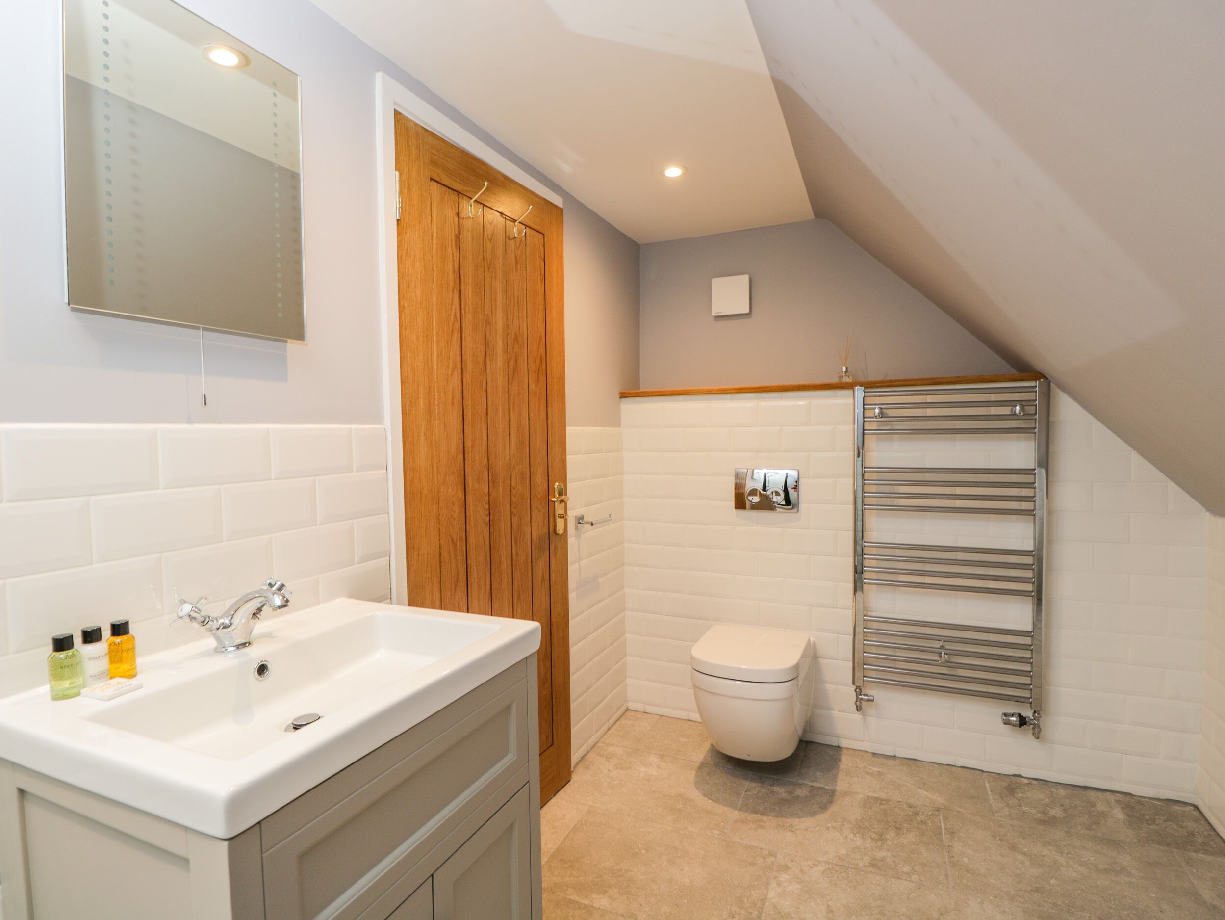A bathroom with a white sink, wooden door, white toilet, and a towel rack.