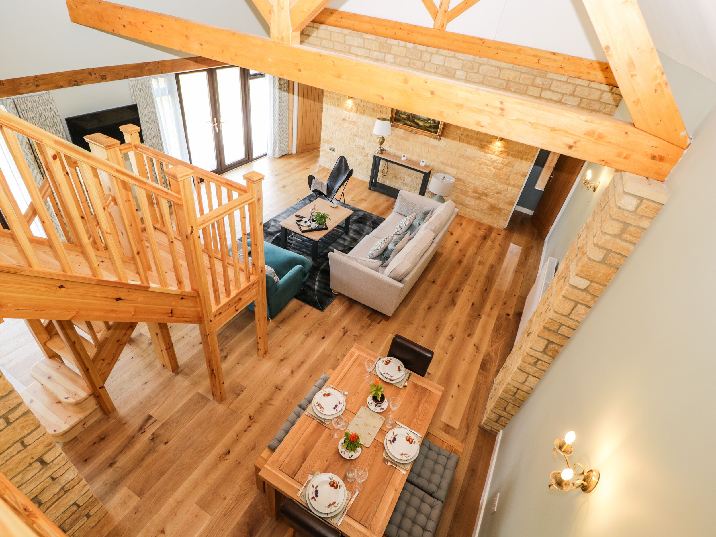 Un loft espacioso con una escalera de madera, una zona de estar acogedora con sofá y sillones, una mesa de comedor preparada para cuatro personas y una chimenea.