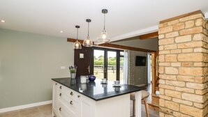 A kitchen with a central island, pendant lights, a stone accent wall, and a view of the outdoors. - Petals Patch (Cheltenham)