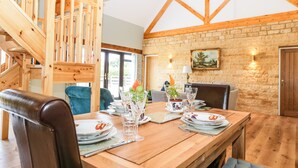 A dining area with a wooden table set for four, surrounded by chairs. A staircase with wooden railings is visible in the background. - Petals Patch (Cheltenham)