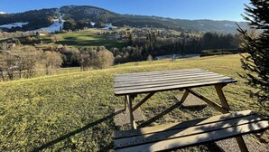 A picnic table on a grassy hill with a view of a village and mountains in the background.