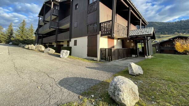 A modern two-story building with balconies, a covered entrance, and a mountainous backdrop.