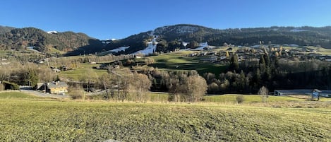 Et smukt landskab med et bjergrigt område og en landsby i dalen, en træbænk i forgrunden og en klar blå himmel.