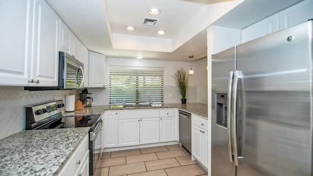 A modern kitchen with white cabinets, a stainless steel refrigerator, a built-in oven, and a granite countertop. - LUXURY Living 4 (Yuma)