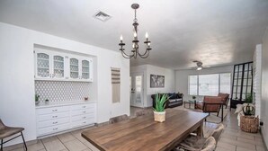 A spacious dining area with a wooden table and chairs, a white cabinet with glass doors, and a hanging chandelier. - LUXURY Living 4 (Yuma)