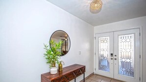A hallway with a wooden console table, a potted plant, a round mirror, and a door with decorative glass panels. - LUXURY Living 4 (Yuma)