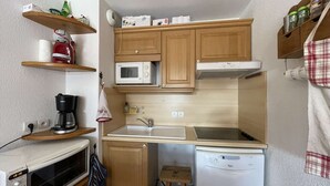 Cocina compacta con armarios de madera, microondas, cafetera, lavaplatos y lavabo.