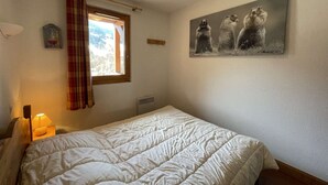 Un dormitorio con cama, ventana con vistas, radiador y un cuadro en la pared.