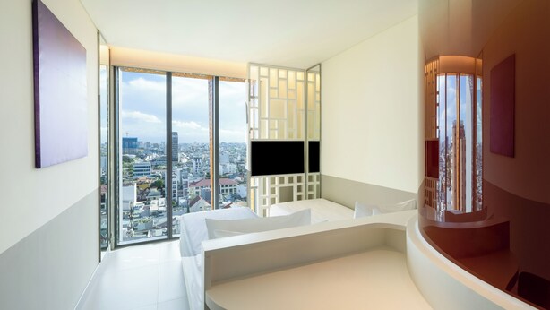 A modern hotel room with a large window offering a city view, a curved white bed, and a built-in TV. - Wink Danang Centre, Unscripted by Hyatt - 24 Hours stay (Da Nang)