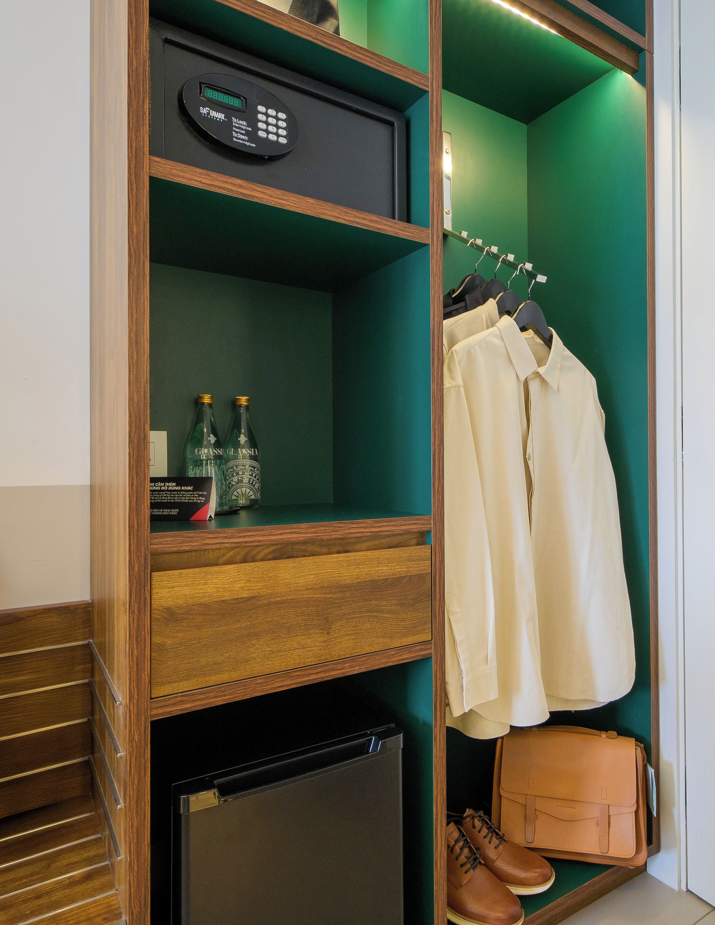 A wooden wardrobe with a built-in safe, a mini fridge, and a hanging shoe rack.