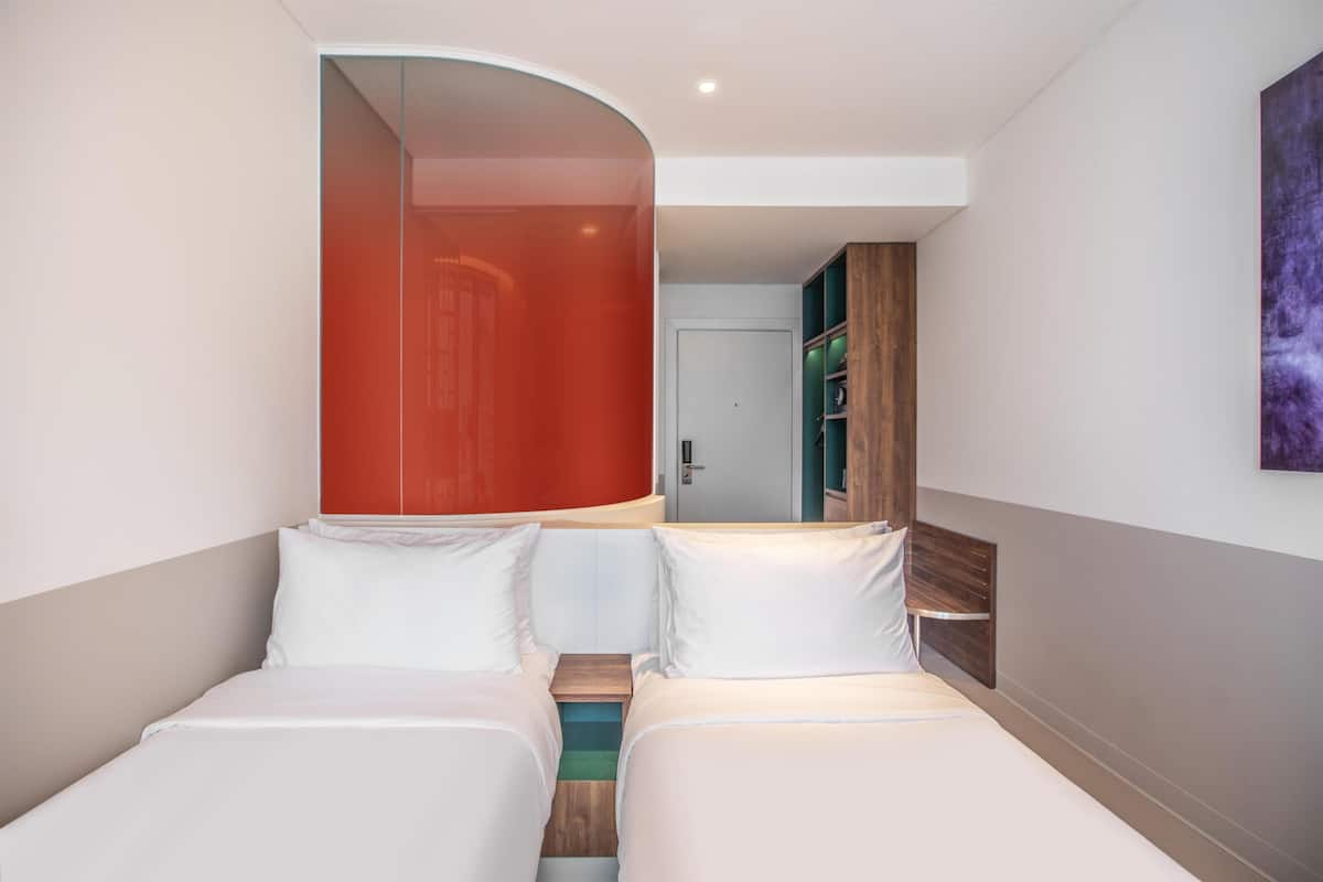 Een hotelkamer met twee bedden, een gebogen spiegel, een houten kast en een deur naar een andere kamer.