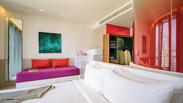 A modern hotel room with a large bed, a sofa, a mirror, and a view of the city through a window.