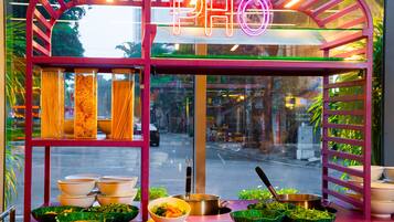 A food stall with a neon sign, glass containers of noodles, bowls, and a pot on the counter.