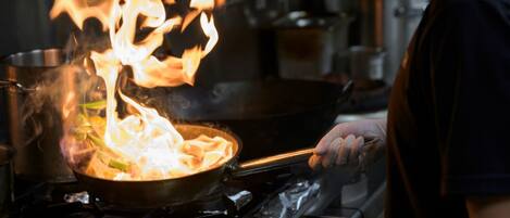 Un chef cuisinant avec des flammes dans une cuisine professionnelle.