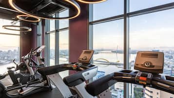 Een sportschool met trainingsapparatuur en grote ramen met uitzicht op de stad.