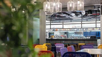L’intérieur d’un restaurant avec un bar, des tables et des chaises aux couleurs vives, et des lampes suspendues.