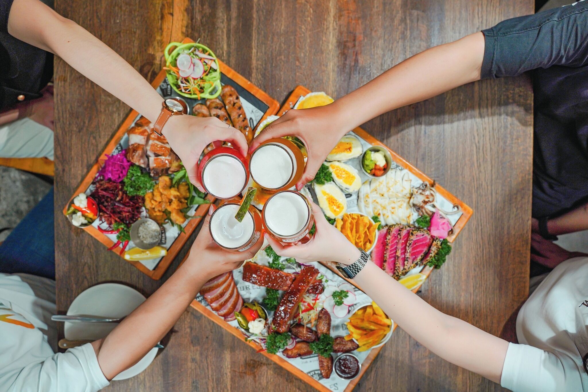 Un groupe de personnes est réuni autour d’une grande table en bois, sur laquelle on trouve une variété de plats et de boissons.