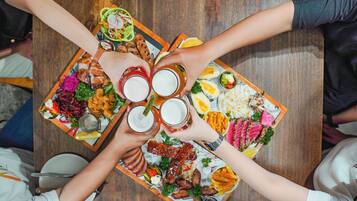 A group of people around a large wooden table with a variety of foods and drinks.