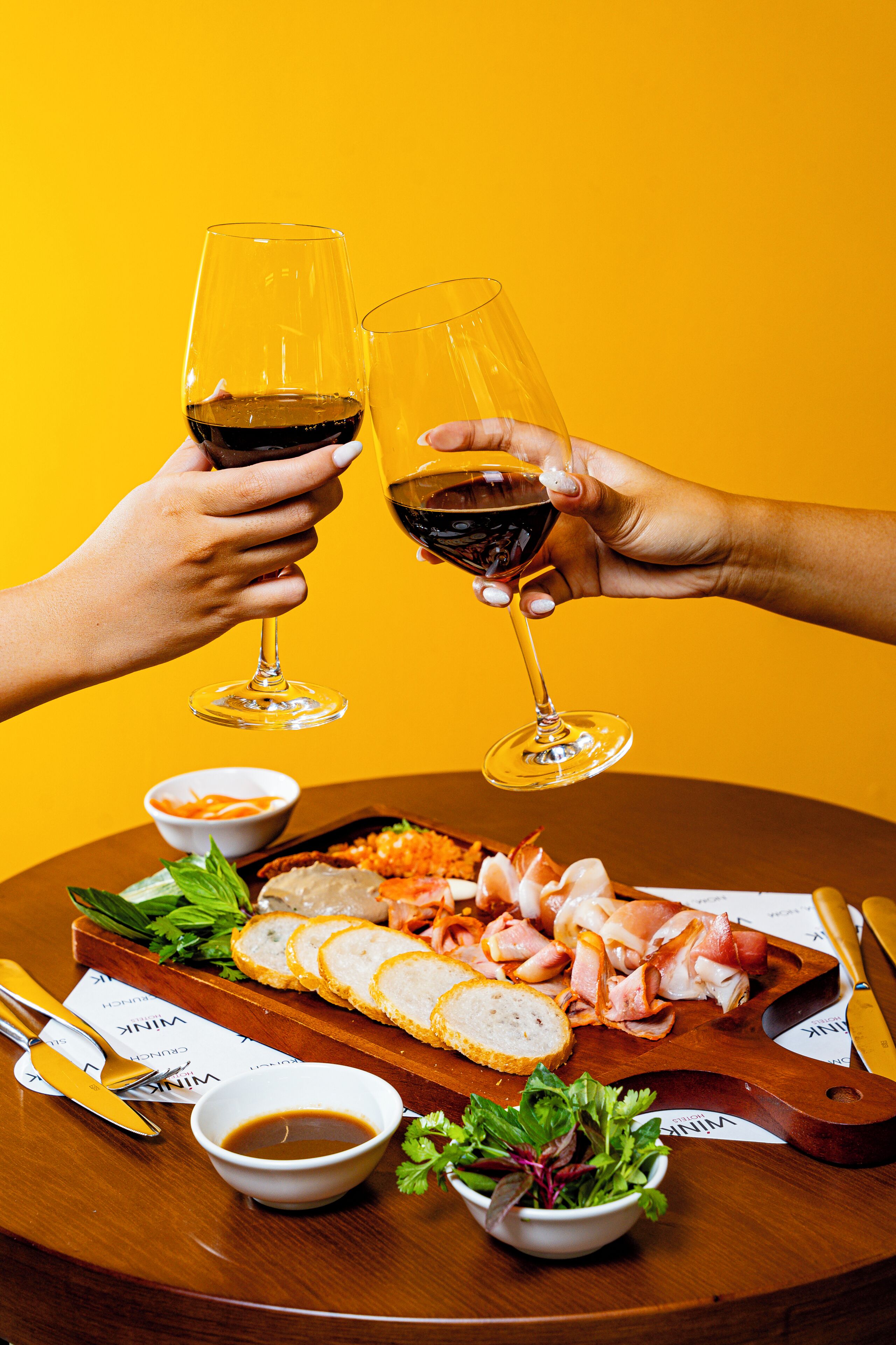 A round wooden table with a charcuterie board, two glasses of red wine, and a bottle of white wine.